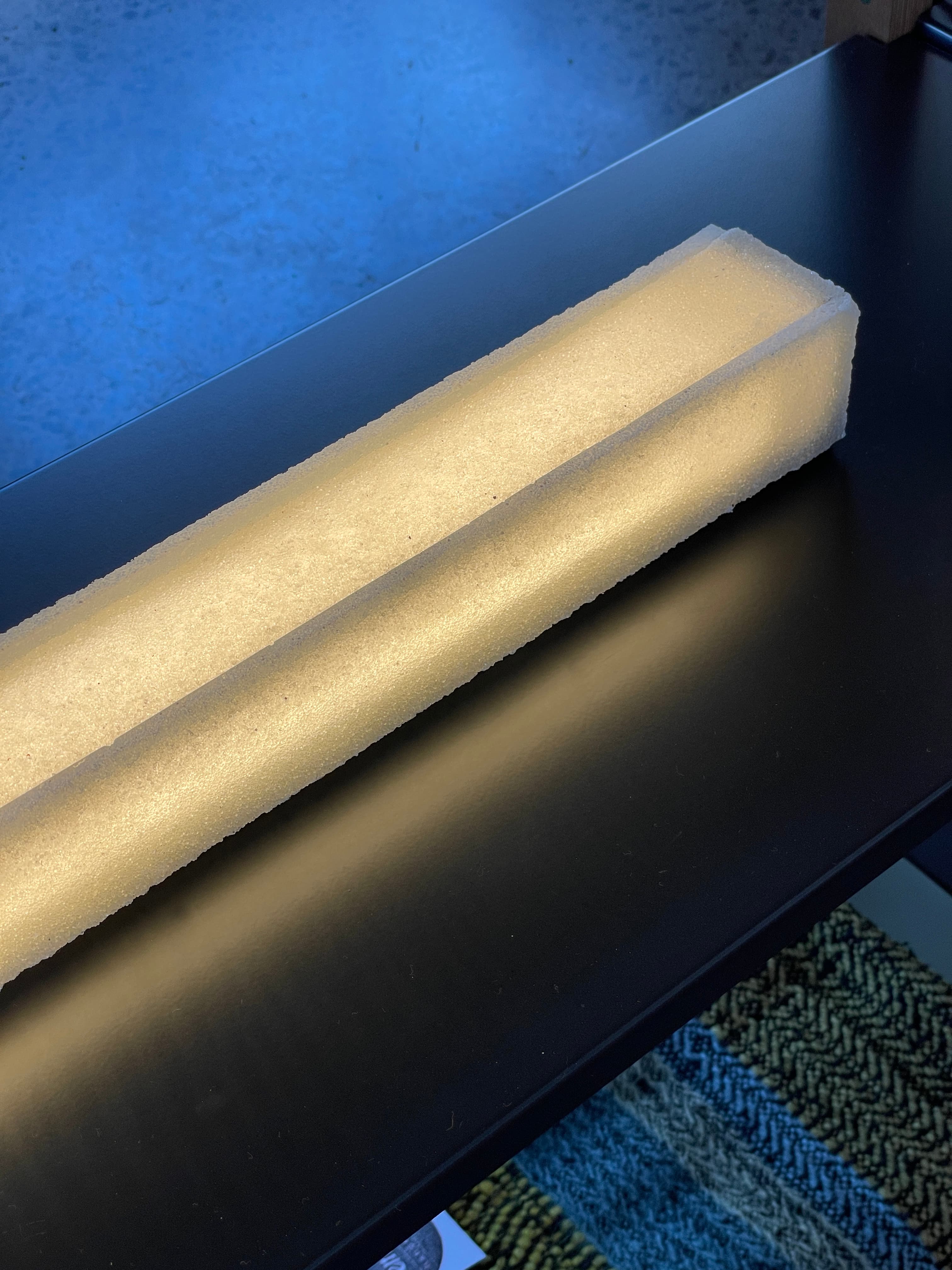 Two illuminated translucent glass bars on a dark metal surface